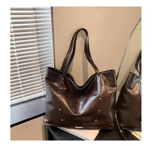 Dark brown faux-leather tote with glossy finish and silver studs, displayed beside a mirror