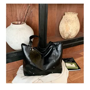 Close-up of a black glossy faux-leather bag with metal studs and a fluffy pom-pom charm