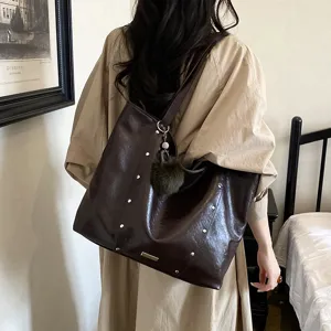 Dark brown faux leather large tote shoulder bag with stud details and pom-pom, modeled from behind