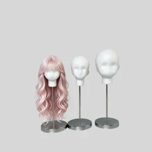 Three foam mannequin heads on metal stands, with a pink long curly wig and bangs on the left