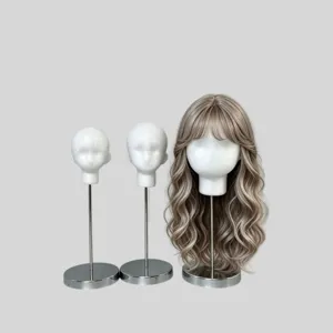 Three foam mannequin heads on metal stands, one wearing a long taupe-gray wavy wig with airy bangs