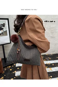 Zijaanzicht van een model met een grijze tas met fijne strepen, bruine pompon en leren kwast