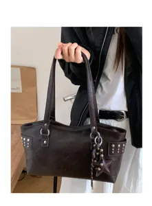 Modelo lleva un bolso marrón oscuro efecto piel, con tachuelas, anillas metálicas y colgante de estrella