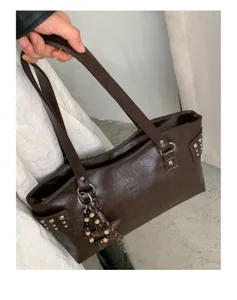 Detalle de bolso marrón efecto piel con tachuelas, aro metálico, estrella colgante y cuentas de madera