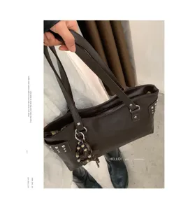 Bolso marrón oscuro en mano, con asas dobles, tachuelas, anillas y colgante de cuentas
