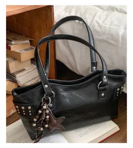 Detalle de un bolso negro de polipiel con tachuelas y colgante de estrella, junto a libros
