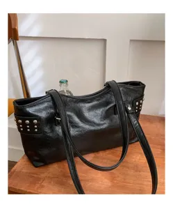 Detalle del acabado negro brillante, los remaches plateados y las largas asas de la bolsa