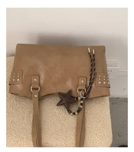 Detalle de bolso marrón de polipiel con tachuelas, asas dobles, estrella colgante y cadena de cuentas