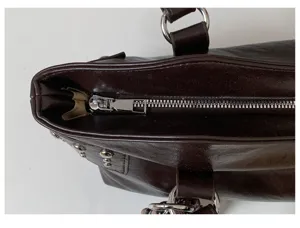 Primer plano de un bolso de cuero sintético marrón oscuro con cremallera, remaches y enganche metálico