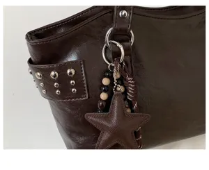 Detalle de bolso de polipiel marrón oscuro con tachuelas, anillas plateadas y colgante de estrella