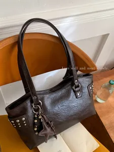 Tote de polipiel marrón oscuro con asas dobles, tachuelas laterales y un colgante de estrella