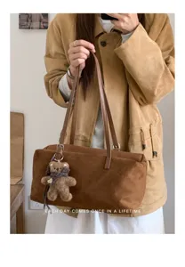 Bolso marrón efecto ante con asas de piel y colgante de osito, en tonos cálidos.