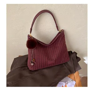 Detail van de bordeauxrode tas met fijne strepen, leren rand, zachte pompon en kettingbedeltje op een jas
