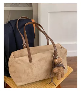 Bolso beige efecto ante, asas marrones y colgante de osito de peluche sobre una silla de madera