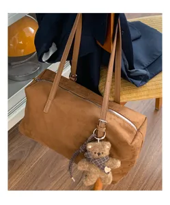 Bolso marrón de ante con asas de piel, cremallera plateada y colgante de oso con bufanda de cuadros