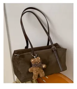 Detalle de un bolso marrón efecto ante, con correa de cuero ajustable y adorno de osito de peluche