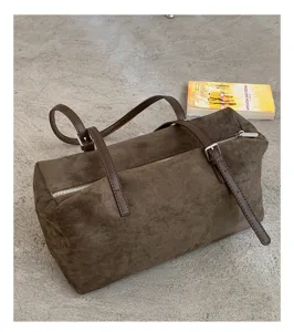 Detalle de un bolso marrón efecto ante, con correas de cuero y herrajes metálicos sobre cemento