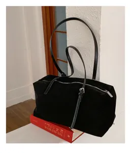 Bolso negro efecto ante, con cremallera superior y correa ajustable, sobre un libro rojo