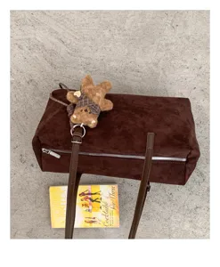 Vista superior de un bolso marrón de ante sintético, con cremallera y colgante de oso de peluche
