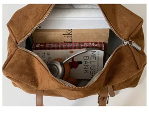 Vista superior de un bolso marrón abierto con aspecto de ante, libros y auriculares en el interior