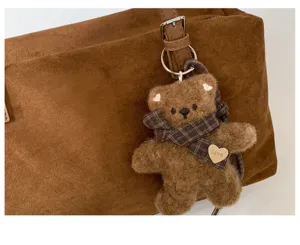 Primer plano de un osito de peluche marrón, bufanda a cuadros y corazón «love» en el bolso