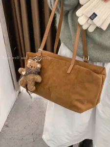 Bolso tote grande de ante marrón, con correas de piel, hebillas metálicas y un colgante de osito