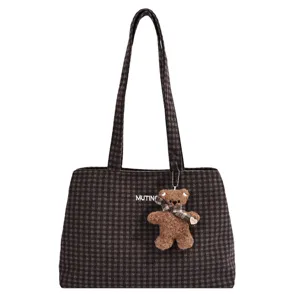 Front view of a brown checked tote with long handles, a teddy bear charm, and MUTINO lettering