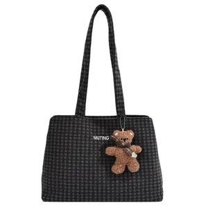 Front view of a charcoal plaid tote with a brown plush bear charm and visible MUTING lettering