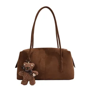 Detalle de un bolso marrón de aspecto ante, con asas largas y un colgante de osito de peluche