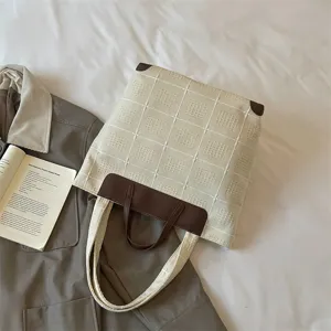 Cremeweiße Tasche mit geprägtem Karomuster und braunen Ledergriffen in flacher Ansicht
