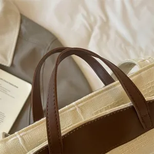 Nahaufnahme einer cremefarbenen Tasche mit Webstruktur, dunkelbraunen Kunstledergriffen und Besatz