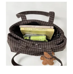 Top-down view into an open brown plaid tote showing black lining, zip closure, books and umbrella.