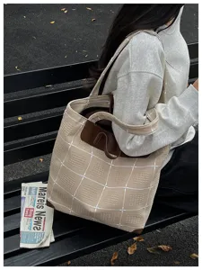 Beige karierte Canvas-Tasche mit dunkelbraunem Besatz, über der Schulter an einer Bank