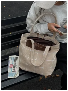 Beige karierte Tragetasche mit Struktur und braunen Griffen auf einer Parkbank im Alltag