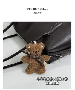 Detalle de bolso de piel sintética oscura con oso de peluche, bufanda de cuadros y dije de corazón