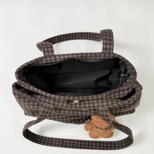 Top view of an open brown plaid bag showing its black lining, zip closure, straps and teddy charm