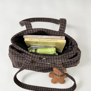 Overhead view of an open brown plaid tote holding books and a phone, with a small bear charm