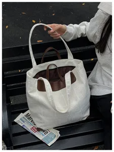 Weiß karierte Tasche mit braunem Besatz, von einer sitzenden Person auf einer Bank gehalten