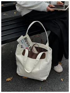 Weiße Tasche mit Prägestruktur, braunen Details, zwei Henkeln und offenem Innenfach