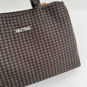 Angled close-up of a dark brown and gray checked fabric bag with white MUTING lettering