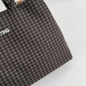 Close-up of dark brown and gray checked tote fabric with partial white embroidered lettering