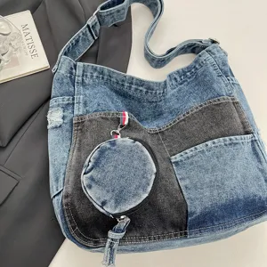Angled view of blue and charcoal patchwork denim with a round coin pouch and adjustable strap