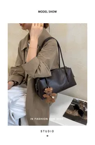 Modelo con un bolso marrón oscuro al hombro, asas largas y un pequeño colgante de osito
