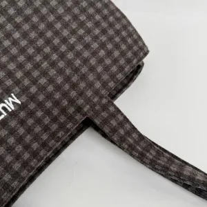 Close-up of dark brown checked fabric, matching handle and partial white embroidered lettering