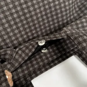Close-up of dark brown and gray checkered fabric with a metal snap fastener and black lining