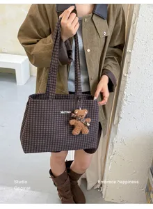 Street-style view of a brown checked tote carried by hand, with a plush teddy bear charm