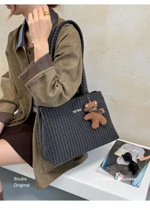 Lifestyle view of a dark checked tote worn on the shoulder with a small teddy bear charm