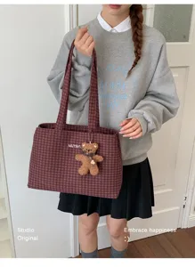 Model carrying a burgundy plaid bag with a small brown teddy bear charm in a casual outfit.