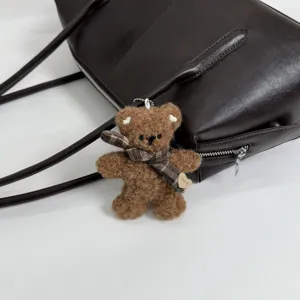 Osito marrón de peluche con bufanda de cuadros y etiqueta de corazón junto a un bolso de cuero