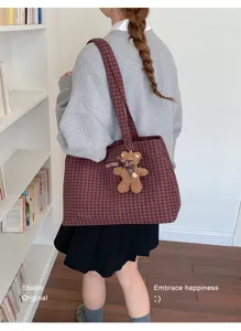 Back view of a model carrying a red checked tote with a plush brown bear charm on its long strap